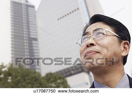 Stock Image - Low angle view of a businessman looking up thinking. Fotosearch