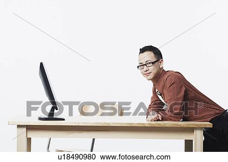 Stock Image - Portrait of a businessman leaning against a table and smiling. Fotosearch