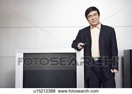 Stock Photo - Portrait of a businessman standing by the side of a television smiling. Fotosearch