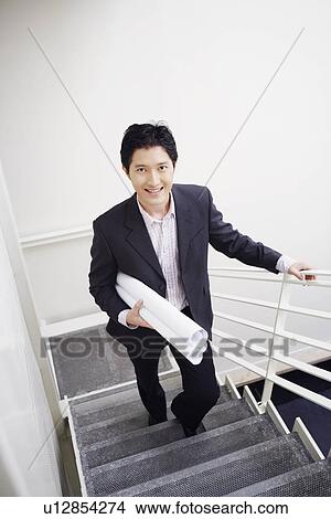 Picture - Portrait of a businessman walking up stairs and carrying blueprints. Fotosearch