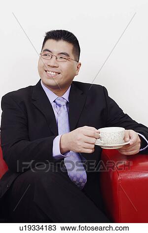 Close-up of a businessman sitting on a couch with a cup of tea and smiling View Large Photo Image Stock Image - Close-up of a businessman sitting on a couch with a cup of tea and smiling. Fotosearch