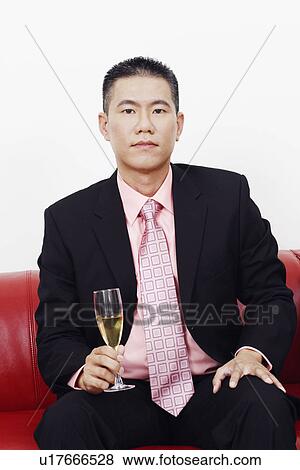 Portrait of a businessman sitting on a couch and holding a champagne flute View Large Photo Image Stock Photo - Portrait of a businessman sitting on a couch and holding a champagne flute. Fotosearch