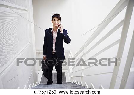 Stock Photo - Portrait of a businessman standing on a staircase and talking on a mobile phone. Fotosearch