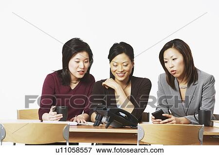 Three businesswomen sitting on chairs looking at the telephone View Large Photo Image Stock Photo - Three businesswomen sitting on chairs looking at the telephone. Fotosearch