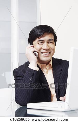 Stock Photography - Businessman sitting in front of a laptop talking on a mobile phone. Fotosearch