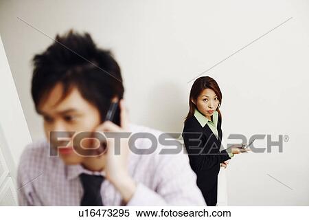 Close-up of a businessman talking on a mobile phone with a businesswoman standing in the background View Large Photo Image Stock Photography - Close-up of a businessman talking on a mobile phone with a businesswoman standing in the background. Fotosearch