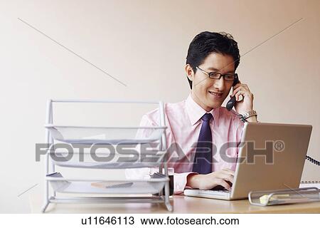 Stock Image - Close-up of a businessman using a laptop and talking on the telephone. Fotosearch