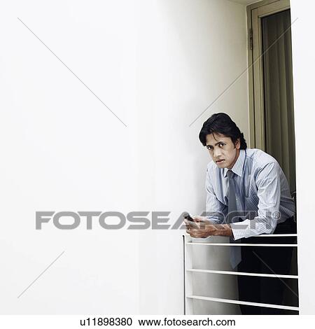 Stock Image - Portrait of a businessman leaning over a railing and holding a mobile phone. Fotosearch