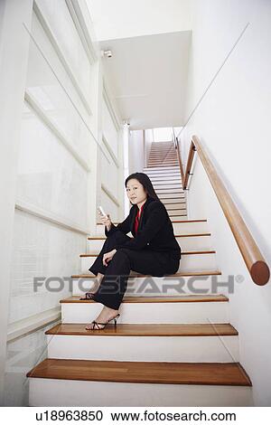 Portrait of a businesswoman sitting on a staircase and operating a mobile phone View Large Photo Image Stock Image - Portrait of a businesswoman sitting on a staircase and operating a mobile phone. Fotosearch