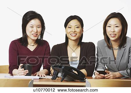 Stock Image - Portrait of three businesswomen sitting and smiling. Fotosearch