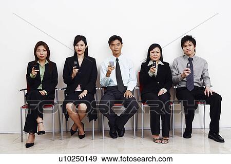 Portrait of two businessmen and three businesswomen sitting together and holding mobile phones View Large Photo Image Stock Photo - Portrait of two businessmen and three businesswomen sitting together and holding mobile phones. Fotosearch