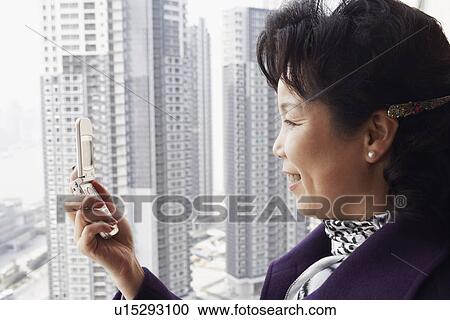 Stock Image - Side profile of a businesswoman looking at a mobile phone smiling. Fotosearch