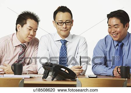 Stock Image - Three businessmen sitting on chairs looking at the telephone. Fotosearch