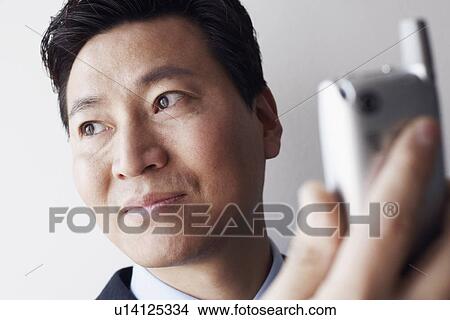 Picture - Close-up of a businessman holding a mobile phone thinking. Fotosearch