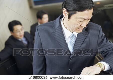 Stock Photography - Close-up of a businessman on an escalator looking at his wrist watch. Fotosearch