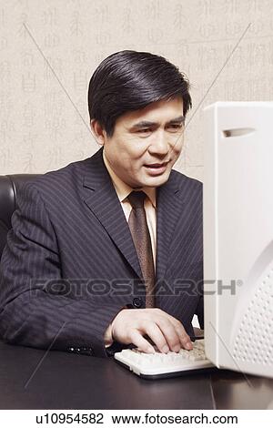 Stock Image - Close-up of a businessman sitting in an office working on a computer. Fotosearch