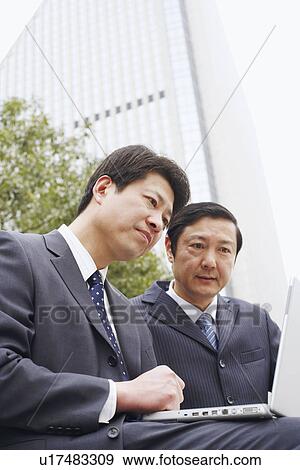 Stock Photo - Low angle view of two businessmen using a laptop. Fotosearch