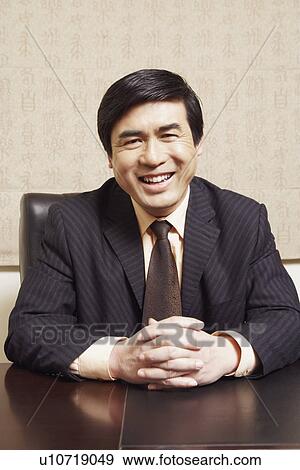 Portrait of a businessman sitting in an office with his hands clasped smiling View Large Photo Image Stock Photo - Portrait of a businessman sitting in an office with his hands clasped smiling. Fotosearch