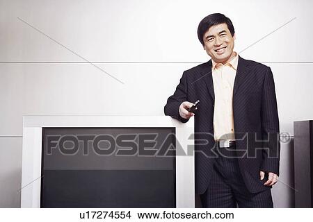 Portrait of a businessman standing by the side of a television smiling View Large Photo Image Picture - Portrait of a businessman standing by the side of a television smiling. Fotosearch