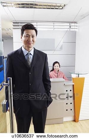Stock Photo - Portrait of a businessman standing in an office with a mature woman wearing a headset. Fotosearch