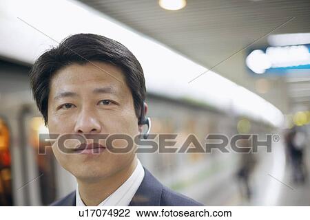 Stock Image - Portrait of a businessman wearing a hands free device at a subway station. Fotosearch