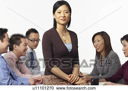Portrait of a businesswoman sitting on a table with business executives sitting behind her View Large Photo Image Stock Image - Portrait of a businesswoman sitting on a table with business executives sitting behind her. Fotosearch