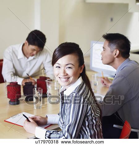 Stock Photo - Portrait of a businesswoman with three business executives seated at a conference table. Fotosearch
