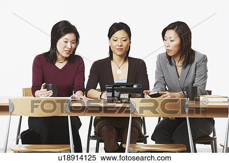 Three businesswomen sitting on chairs looking at the telephone View Large Photo Image Stock Photography - Three businesswomen sitting on chairs looking at the telephone. Fotosearch