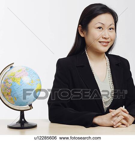 Stock Photograph - Businesswoman sitting in an office with a globe in front of her. Fotosearch