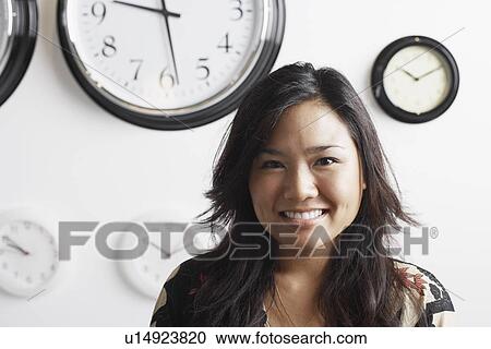 Close-up of a businesswoman smiling standing in front of clocks on the wall View Large Photo Image Stock Image - Close-up of a businesswoman smiling standing in front of clocks on the wall. Fotosearch