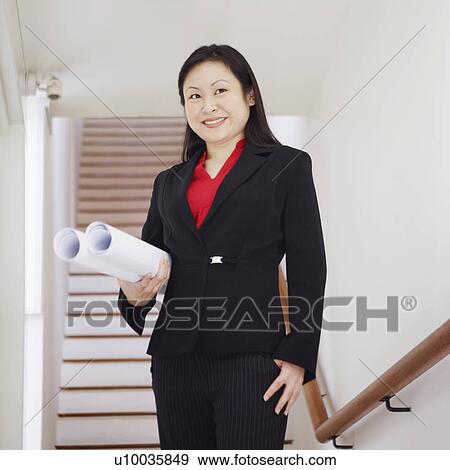 Stock Photo - Low angle view of a businesswoman holding rolled up charts and smiling. Fotosearch