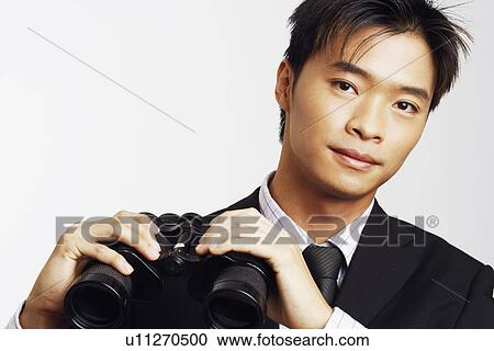 Stock Image - Portrait of a businessman holding a pair of binoculars. Fotosearch