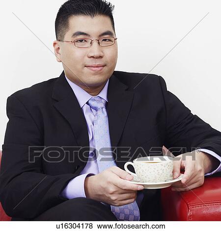 Stock Photo - Portrait of a businessman sitting on a couch with a cup of tea and smiling. Fotosearch