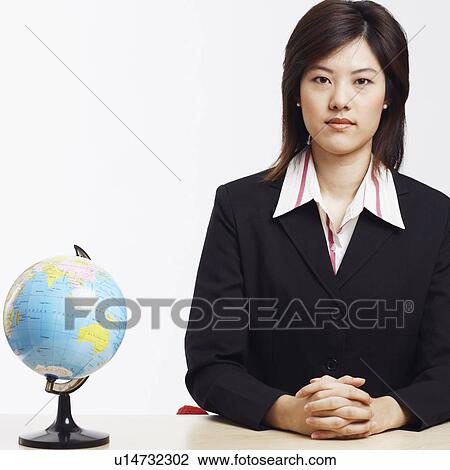 Stock Image - Portrait of a businesswoman sitting with a globe in front of her. Fotosearch