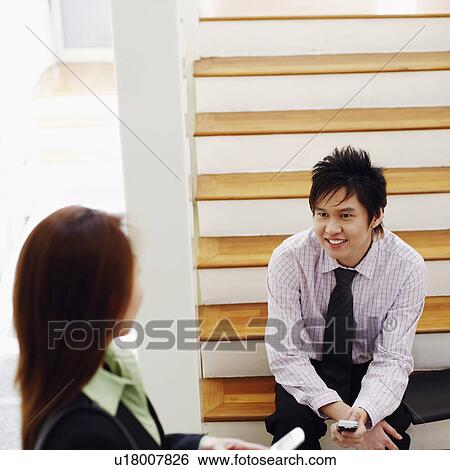 Stock Photograph - High angle view of a businesswoman talking to a businessman and smiling. Fotosearch
