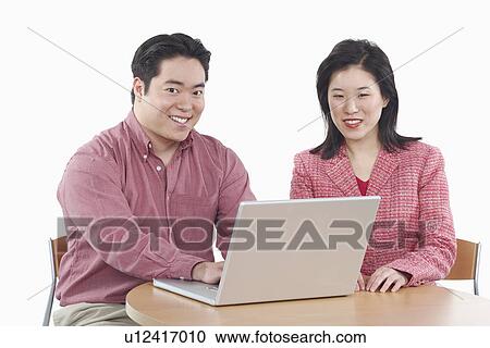 Stock Image - Portrait of a businessman and a businesswoman using a laptop. Fotosearch
