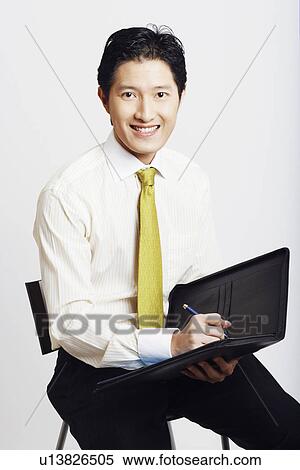 Stock Photography - Portrait of a businessman holding a file with a pen and smiling. Fotosearch