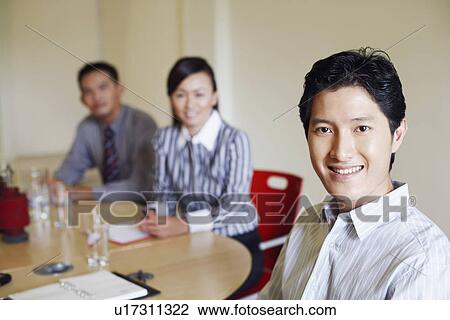 Portrait of a businessman seated at a conference table and smiling with two colleagues View Large Photo Image Stock Image - Portrait of a businessman seated at a conference table and smiling with two colleagues. Fotosearch