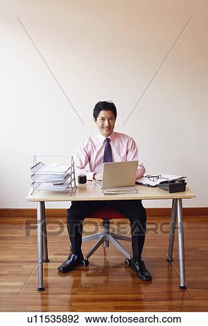 Portrait of a businessman sitting in an office with a laptop and smiling View Large Photo Image Stock Image - Portrait of a businessman sitting in an office with a laptop and smiling. Fotosearch