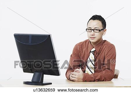Portrait of a businessman sitting in front of a flat screen monitor View Large Photo Image Stock Photo - Portrait of a businessman sitting in front of a flat screen monitor. Fotosearch