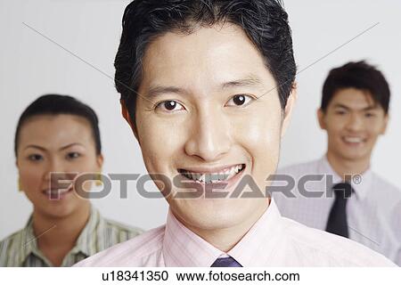 Stock Image - Portrait of a businessman smiling with his colleagues in the background. Fotosearch