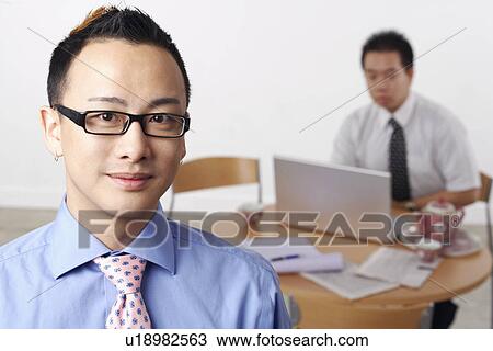 Portrait of a businessman smiling with another businessman using a laptop behind him View Large Photo Image Stock Image - Portrait of a businessman smiling with another businessman using a laptop behind him. Fotosearch