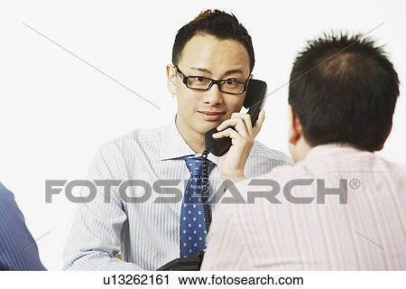 Portrait of a businessman talking on the telephone with two businessmen sitting in front of him View Large Photo Image Stock Image - Portrait of a businessman talking on the telephone with two businessmen sitting in front of him. Fotosearch