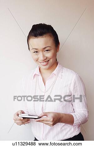 Stock Photo - Portrait of a businesswoman operating a mobile phone and smiling. Fotosearch