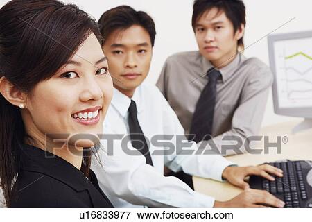 Stock Photo - Portrait of a businesswoman sitting with two businessmen in an office and smiling. Fotosearch