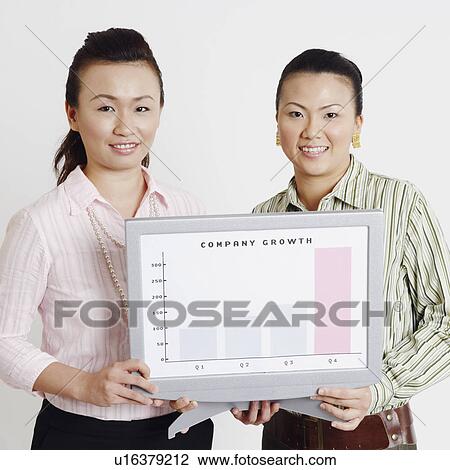 Stock Image - Portrait of two businesswomen holding a progress report and smiling. Fotosearch