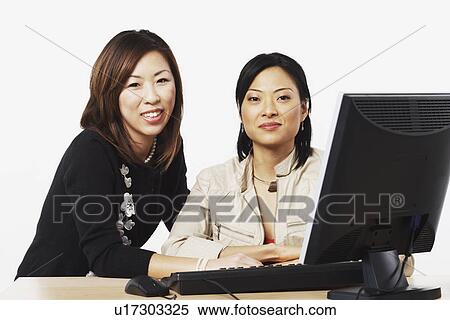 Stock Photography - Portrait of two businesswomen sitting in front of a computer. Fotosearch