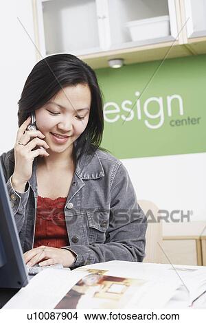 Picture - Close-up of a businesswoman sitting in front of a computer using a mobile phone. Fotosearch