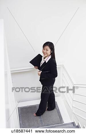 Stock Image - High angle view of a businesswoman standing on the staircase and smiling. Fotosearch