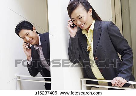 Low angle view of a businessman and a businesswoman talking on mobile phones View Large Photo Image Stock Photograph - Low angle view of a businessman and a businesswoman talking on mobile phones. Fotosearch